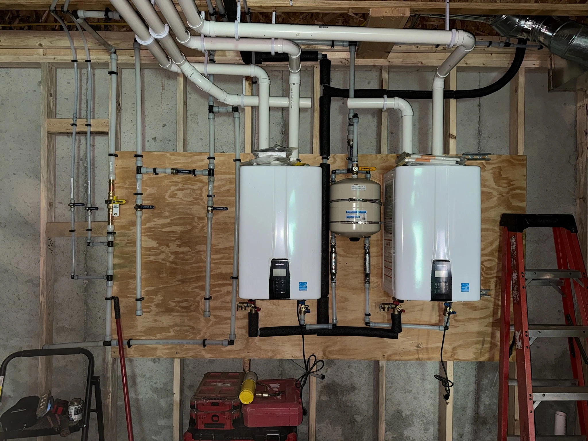 Two wall-mounted water heaters with connected pipes in a basement.